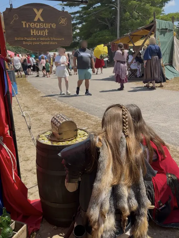 The X Treasure Hunt booth on a faire lane: the sign, a treasure chest on a barrel, and two players in costume