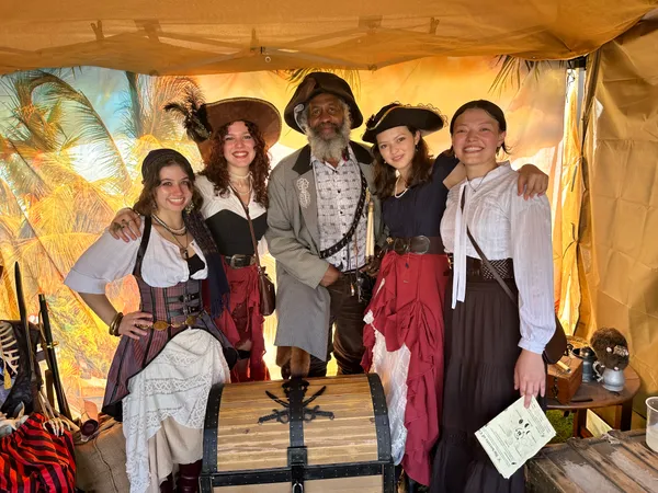 Group of pirates posing with the captain around the treasure chest