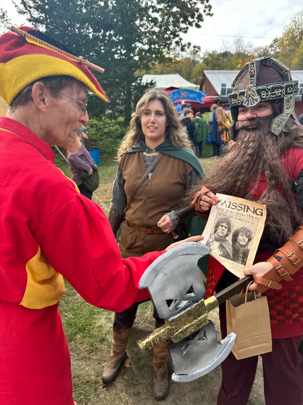 Jester, hobbit, and dwarf cosplayers interacting with a treasure hunt missing poster