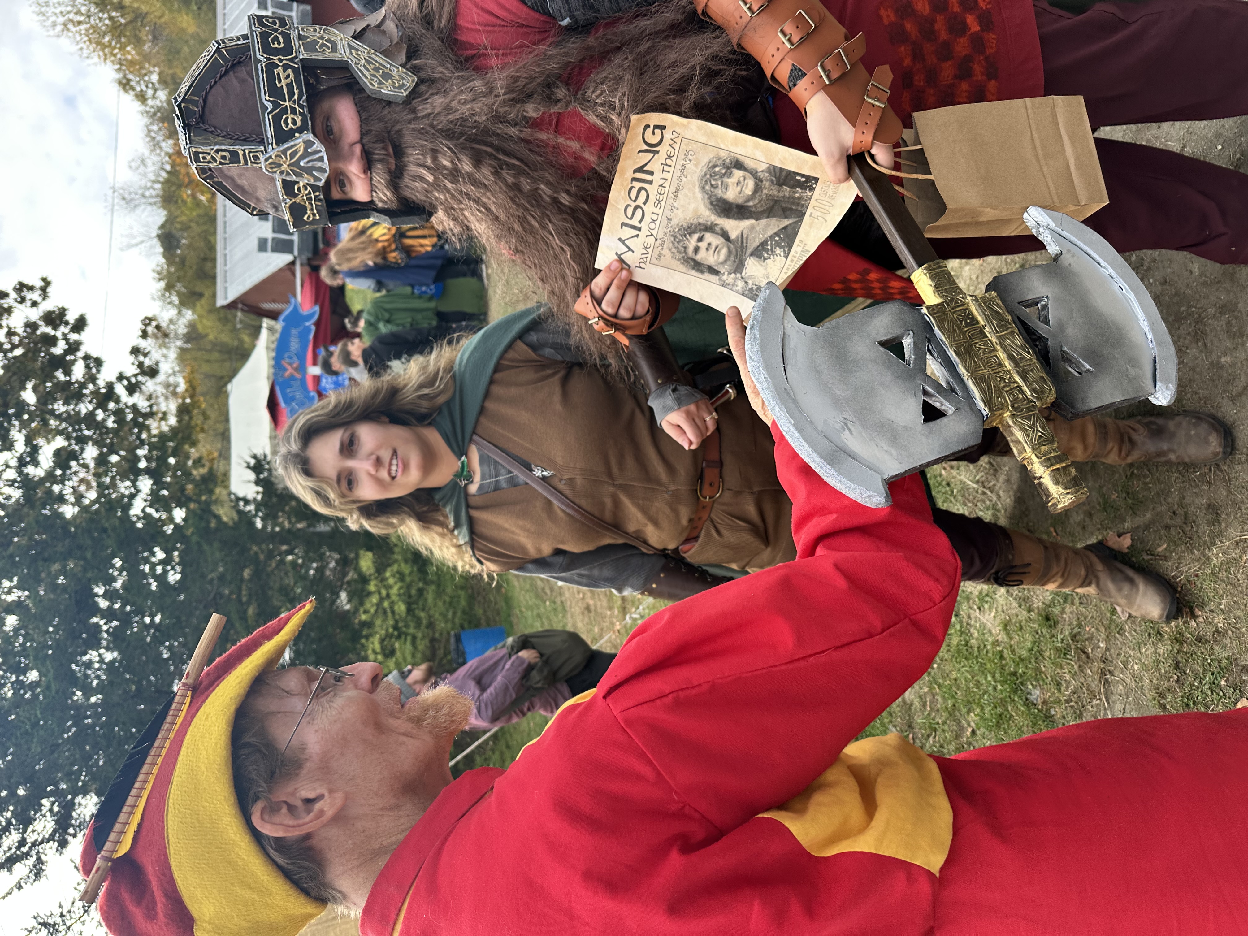 Jester, hobbit, and dwarf cosplayers interacting with a treasure hunt missing poster