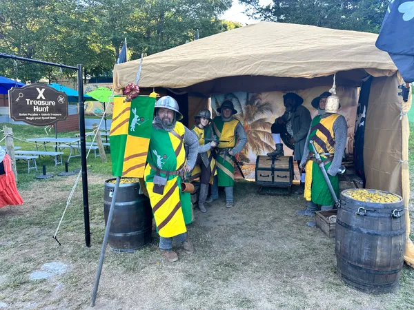Medieval knights in heraldic tabards posing at the X Treasure Hunt booth with treasure barrels