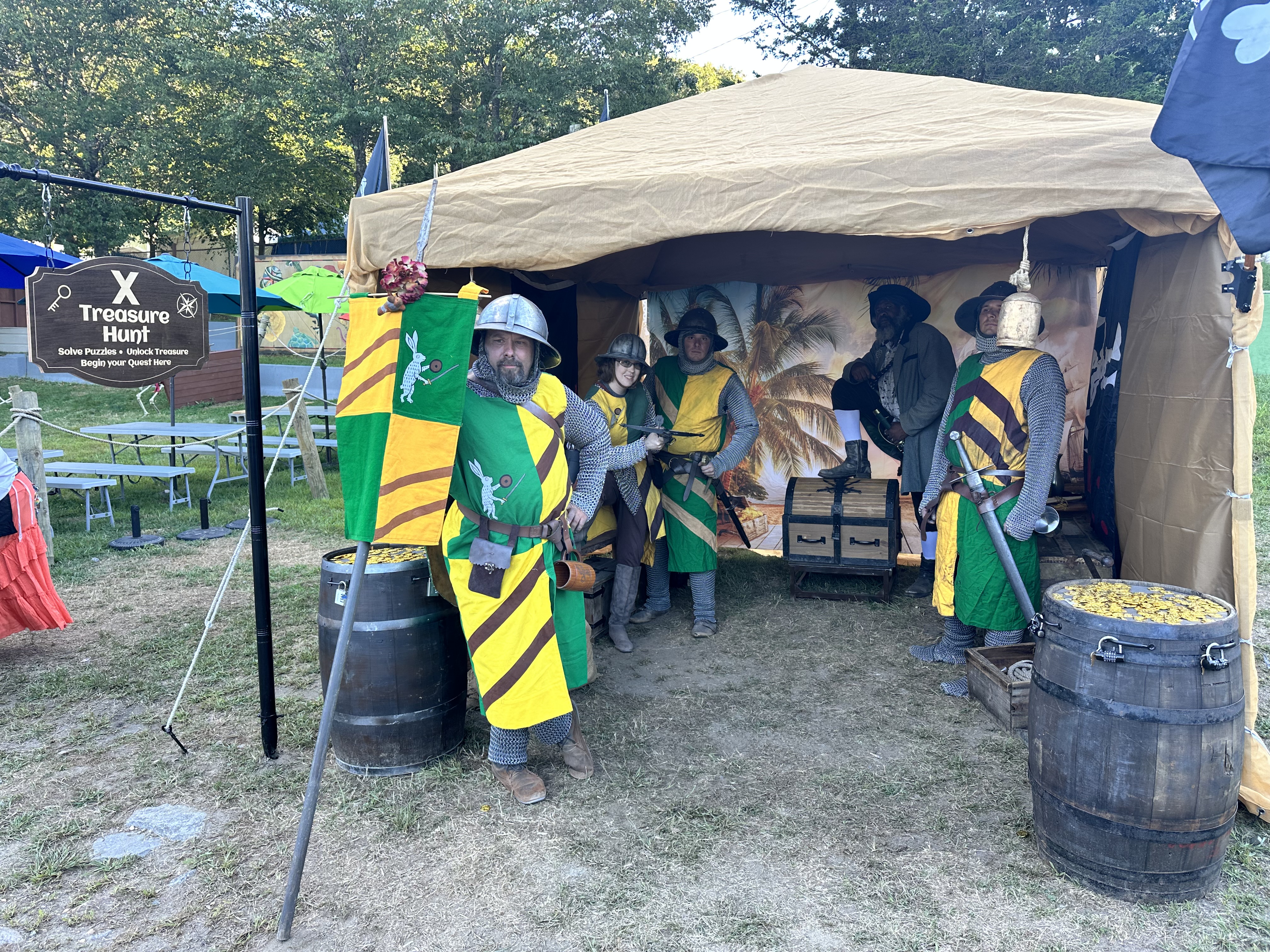 Medieval knights in heraldic tabards posing at the X Treasure Hunt booth with treasure barrels