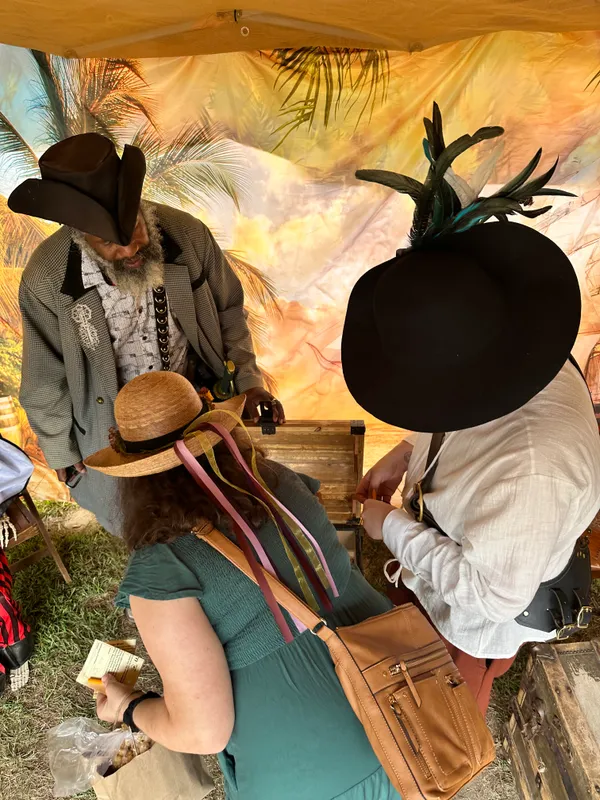 Two participants in Renaissance hats opening the treasure chest inside the pirate tent