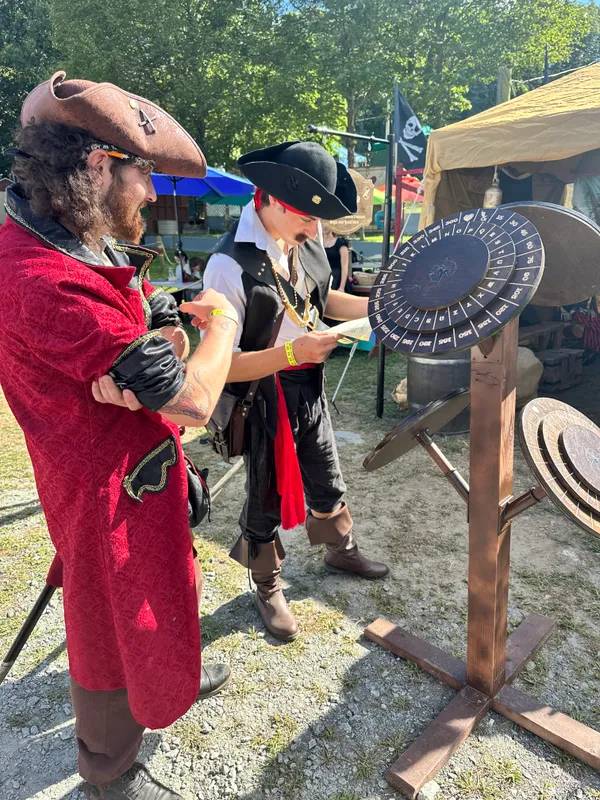 Two pirates in elaborate costumes studying a quest sheet beside the cipher wheel decoder