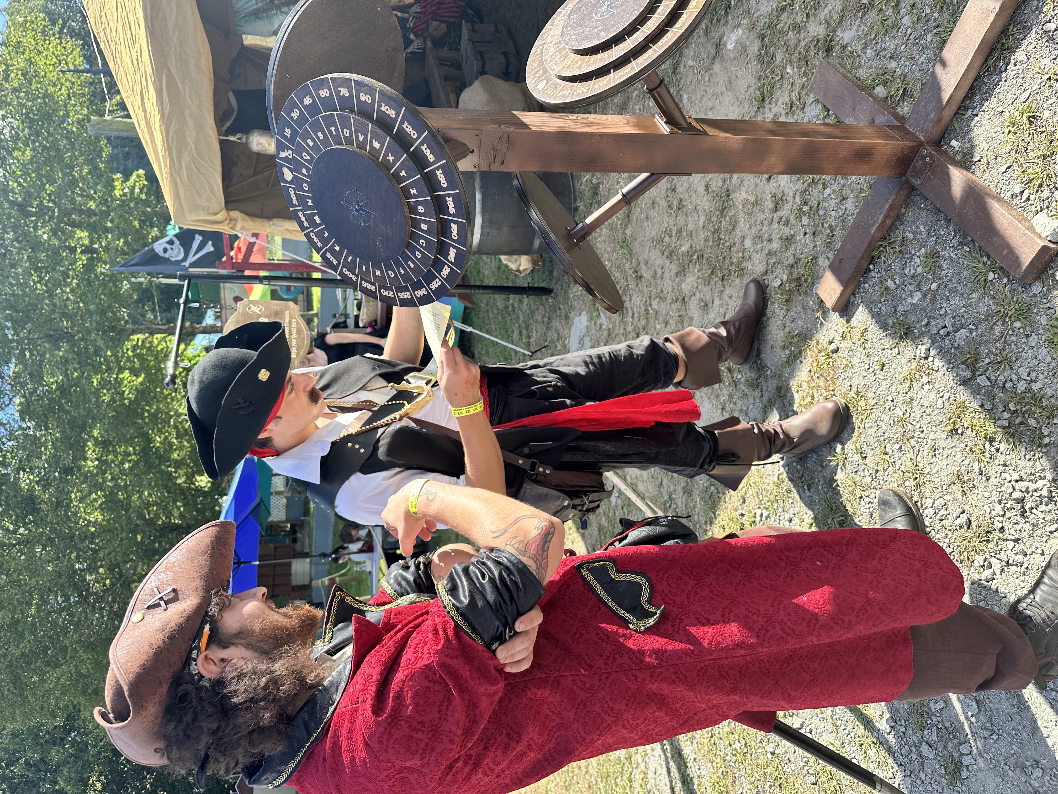 Two pirates in elaborate costumes studying a quest sheet beside the cipher wheel decoder