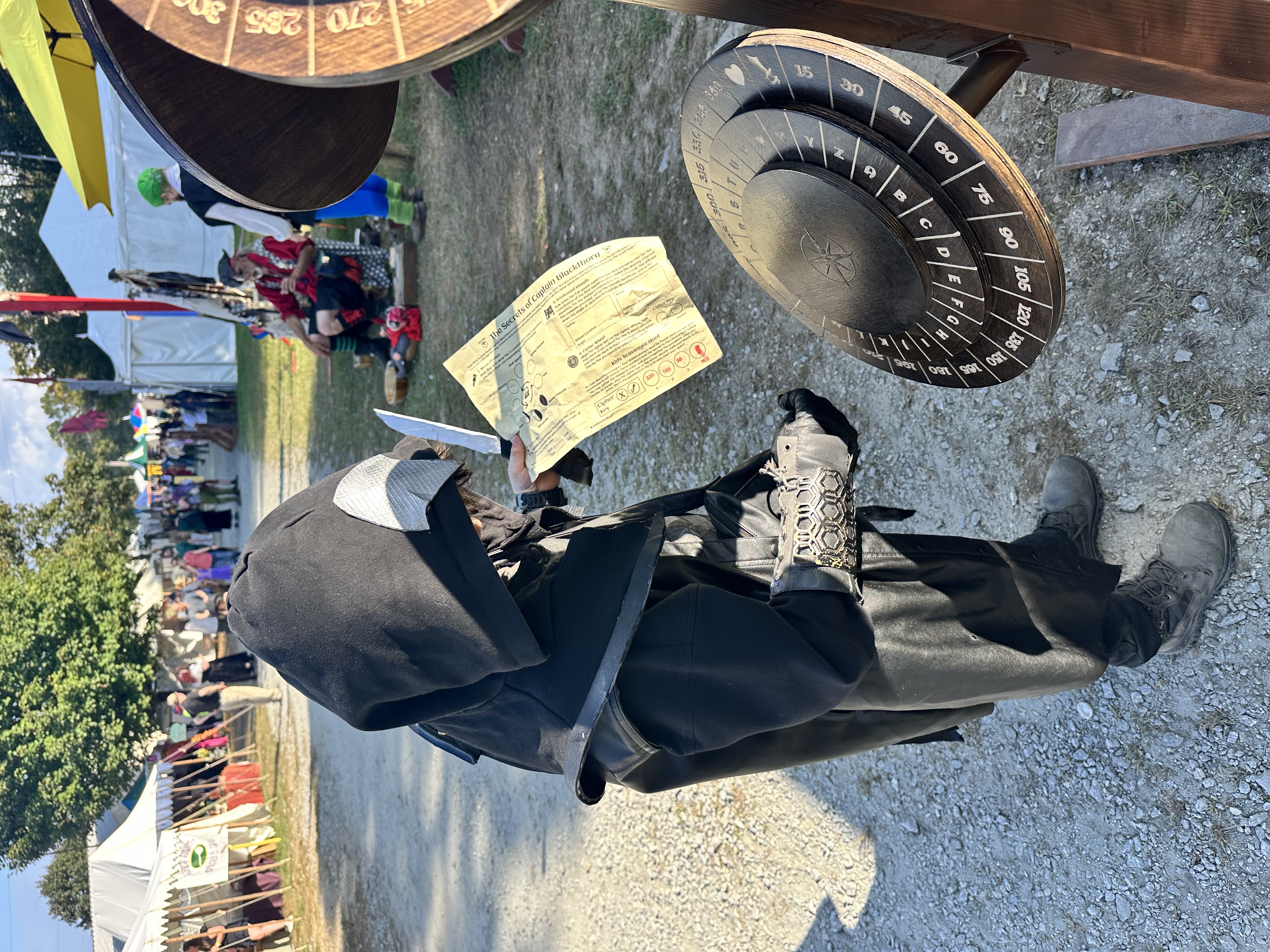 Child in dark assassin costume studying a quest sheet beside the cipher wheel